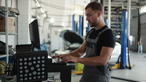 Man at the workshop in uniform use computer for his job for fixing broken car Stock Footage 306807434