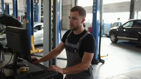Man at the workshop in uniform use computer for his job for fixing broken car Stock Footage 306807470