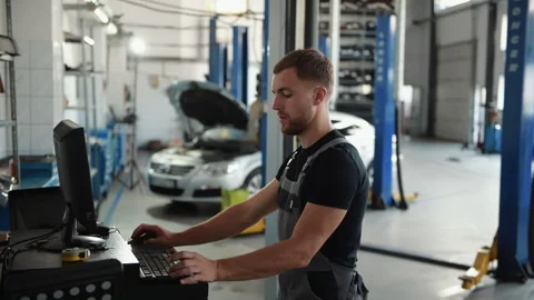 Man at the workshop in uniform use computer for his job for fixing broken car Stock Footage 306807543