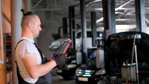 A man in workwear using a tablet computer in automotive garage Stock Footage 275565170