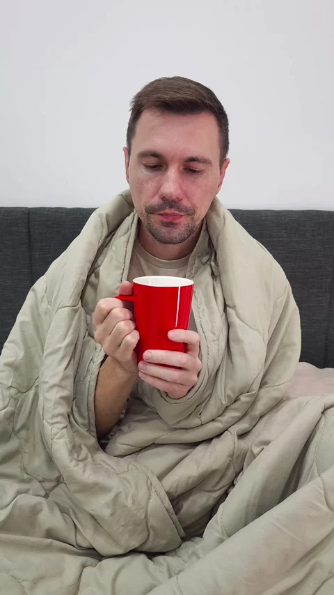 Man wrapped in beige blanket holding red mug. Man Sipping from a Cup Stock Footage 284042953