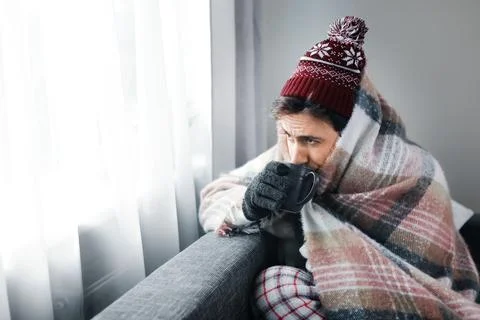 Man wrapped in blanket and hat drinking warm tea at home during energy cris.. Stock Photos