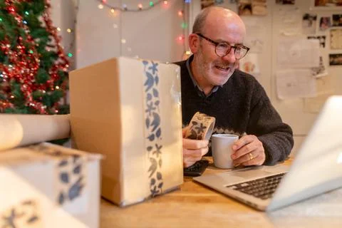 Man wrapping parcels and using laptop Stock Photos