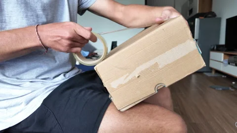 A man wraps a cardboard box with packing tape Vídeos de archivo 331126283