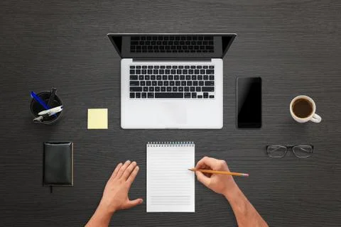 Man write on pad. Top view of work desk with laptop, mobile phone with blank  Stock Photos