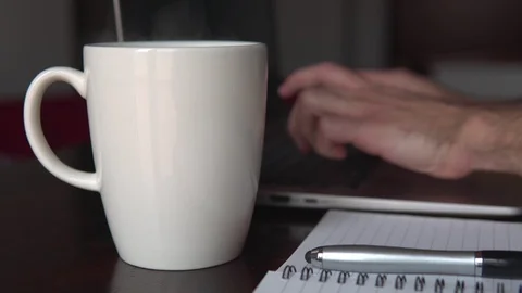 Man writes on the computer and drinks his hot cup while working Stock Footage 129440043