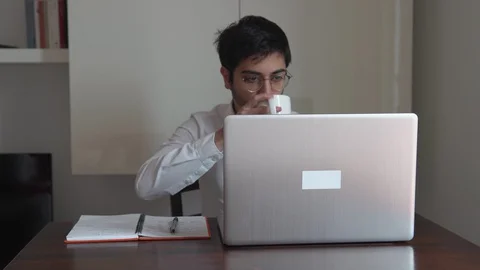 Man writes on the computer and drinks his hot cup while working at his house Stock Footage 129440164