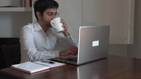 Man writes on the computer and drinks his hot cup while working at his house Stock Footage 129442984
