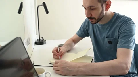 The man writes in his notebook using a pencil. Stock Footage 307666815
