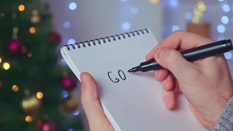 Man writes marker board at white table with Christmas decor goals and plans new Stock Footage 221601907