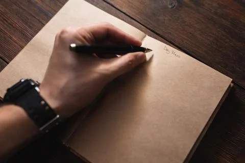 A man writes in a notebook Day plans with a pen on a dark wooden table. Stock Photos