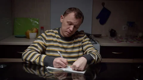 Man writes in a notebook his plans for the future, sitting at the kitchen table Stock Footage 135149371