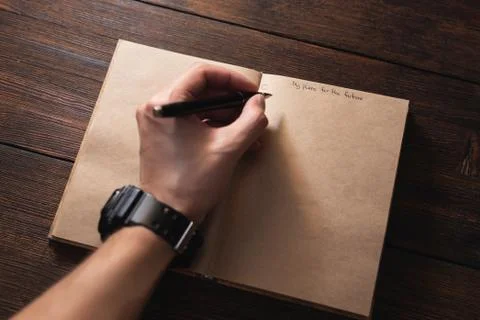 A man writes in a notebook My plans for the future with a pen on a dark table. Stock Photos