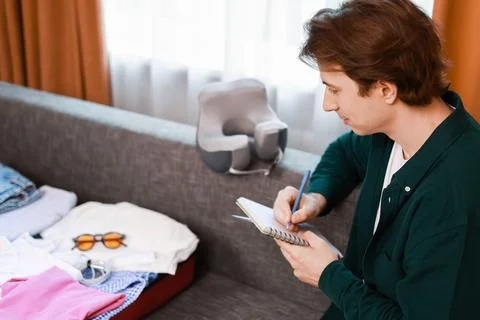 Man writes a packing list in a notebook during travel preparation for a sum.. Stock Photos