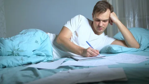A man writes on paper documents lying in bed. work at home. Stock Footage 127855302