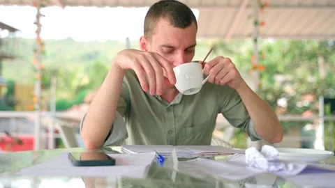 The man writes with a pen in his notebook, takes a mug of coffee and takes a sip Stock Footage 231336781