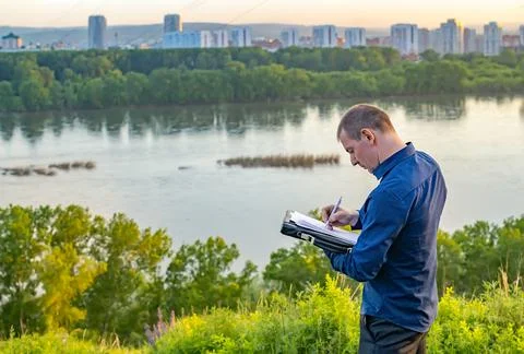 A man writes on a piece of paper while standing on a hill on the shore Stock Photos