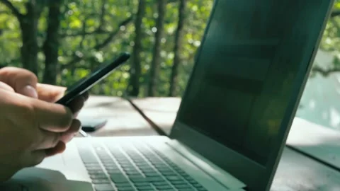 Man writes sms on the phone while working on a laptop in the middle of nature Stock Footage 148320377