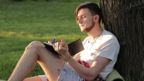 A man writes something in a notebook and ponderes. Poet writes poetry Stock Footage 89182752