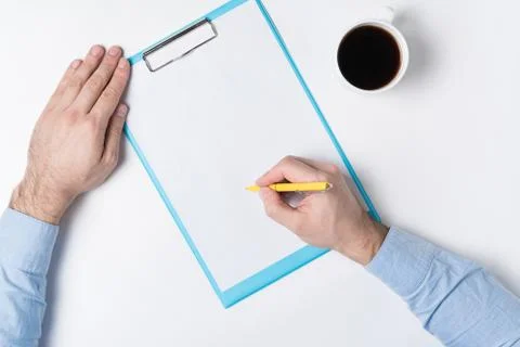 Man writes on white sheet. Top view of man hands, paper and Cup of coffee. Co 스톡 사진