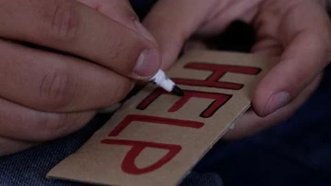 A man writes the word help on a cardboard card with a red felt-tip pen close-up Video stock 189529594