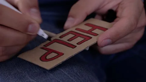 A man writes the word help on a cardboard card with a red felt-tip pen close-up Stock Footage 190080624
