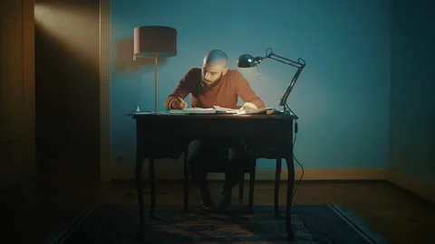 Man writing and searching for notes on a desk with a lamp Stock Footage 135387060
