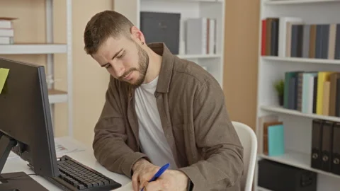 Man writing with blue pen at desktop computer and monitor, leaning forward .. Stock Footage 337365157