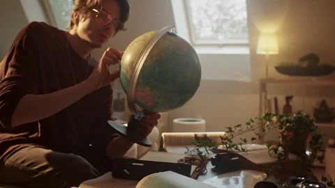Man writing a book while examining a globe in a cozy room setting Stock Footage 319964019
