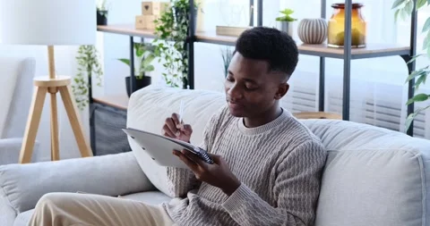 Man writing to do list in notepad sitting on sofa Stock Footage 196077175