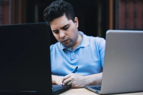 Man writing down data on a paper while trading cryptocurrencies with laptops Stock Photos