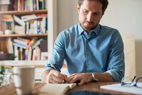Man writing down notes while working in his living room Stock Photos
