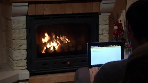 Man Is Writing On A Laptop In Front Of A Fireplace Technology and Home Concept Stock Footage 44015368