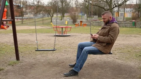 Man writing a message and swinging on the playground  Stock Footage 60962775