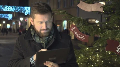 Man writing message next to christmas tree, by tablet app at night, steadycam 库存影片 72782171
