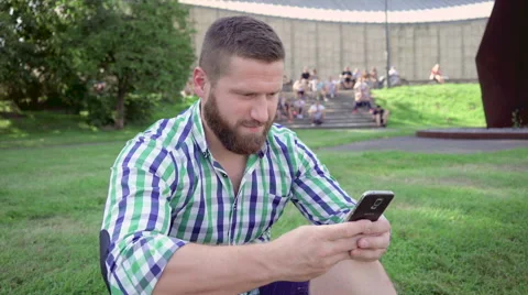 Man writing message on smartphone, sitting on grass. Steadicam. Vídeos de archivo 67236198