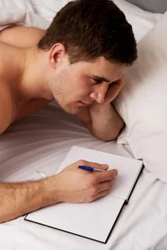 Man writing a note in his bed. Stock Photos