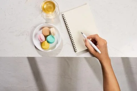 Man writing on notebook with cake macaron and tea mug on white background. Fl Stock Photos