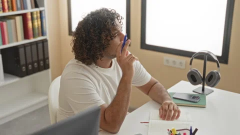 Man writing in notebook at desk in a library building, pen to lips thinking.. Stock Footage 337402846