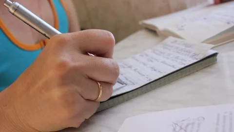 Man writing on notebook at desk with stack of books in foreground - writing a Stock Footage 91227942