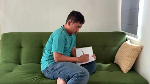 A man writing on notebook pages on sofa. Suitable for study, planning Stock Footage 340323432