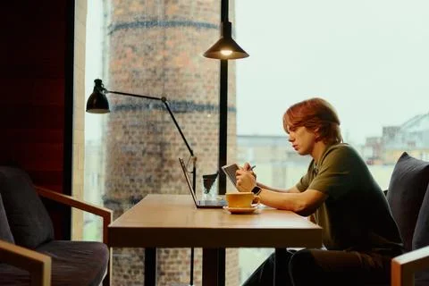 Man Writing in Notebook While Working on Laptop in Cafe Stock Photos