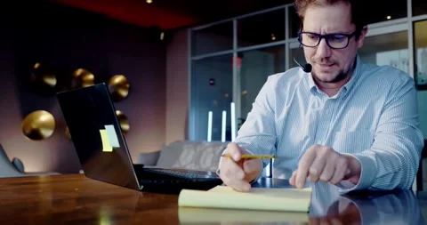 Man Writing Notes at a Desk in an Office Stockbeeldmateriaal 323680879