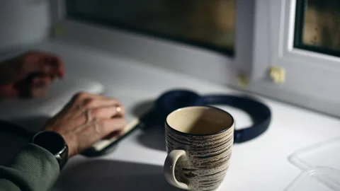 A man writing notes in a notebook beside a striped mug with coffee Video stock 329172319