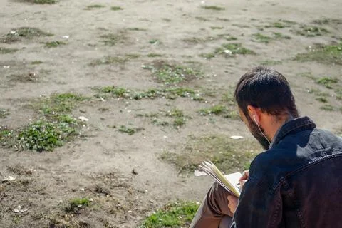 Man writing or drawing on notebook in a park. Stock Photos