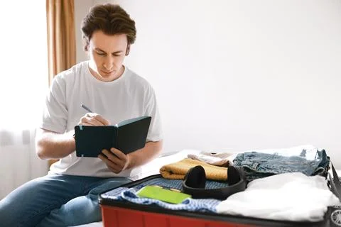 Man writing a packing list in a notebook during travel preparation. He is p.. 写真素材