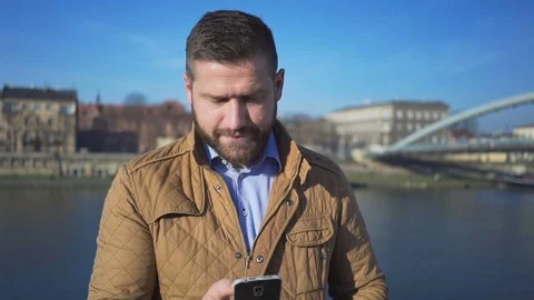 Man writing sms on smartphone app, smiling at camera, river, sunny day 库存影片 72709673
