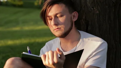 The man is writing something in a notebook. The concept of literature and poetry Stock Footage 89182806