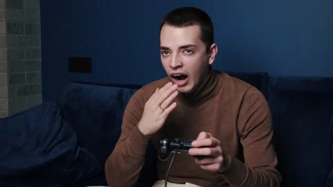 A man yawning while playing a video games joystick controller on sofa at home Stock Footage 144330618