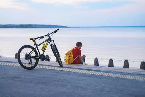 Man with yellow backpack sitting alone by the lake in town. Travelling by Stock-Fotos